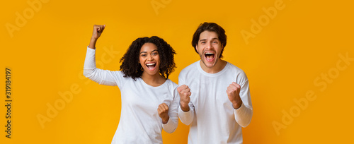 Happy interracial couple rejoicing success, celebrating victory with raised fists
