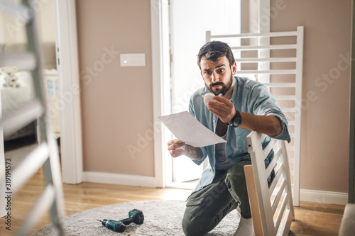 Man reading instructions for assembling a baby crib.