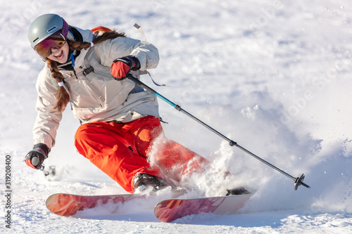 Girl On the Ski. a skier in a bright suit and outfit with long pigtails on her head rides on the track with swirls of fresh snow. Active winter holidays, skiing downhill in sunny day. Woman skier