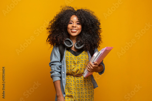 Female student in campus with books in her arms. Yellow background.