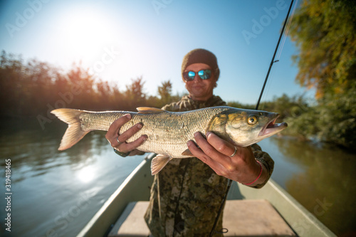 Happy angler holds Asp fish (Aspius aspius) being on the boat and smiles. Astrakhan region, Russia