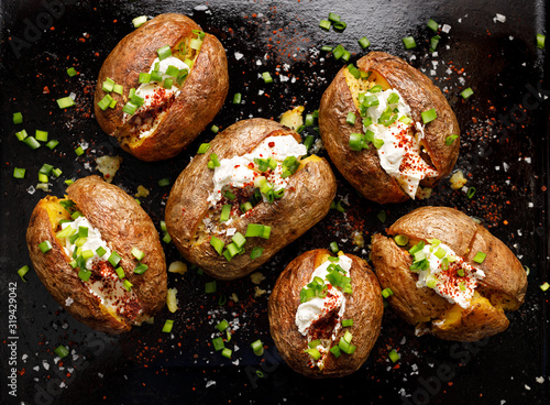 Baked potato, baked potatoes stuffed with butter, cream cheese and green onions, seasoned with freshly ground black pepper and sea salt flakes on a black background, top view