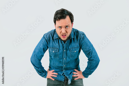 Young man with expression of tiredness and exhaustion. Denim shirt and isolated gray background.