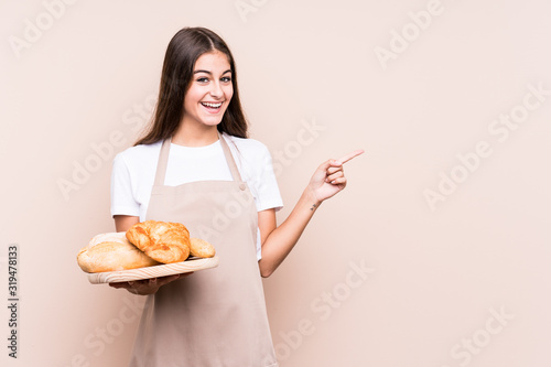 Young caucasian baker woman isolated smiling and pointing aside, showing something at blank space.