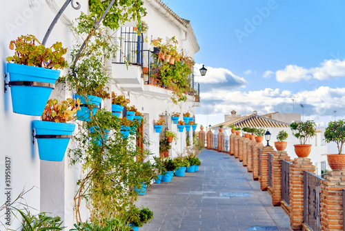 Idyllic scenery empty picturesque street of small white-washed village of Mijas. Path way decorated with hanging plants in bright blue flowerpots, Costa del Sol, Andalusia, Province of Málaga, Spain.