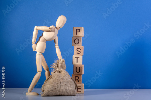 Wooden mannequin with a bag near the tower of cubes with the inscription Posture.