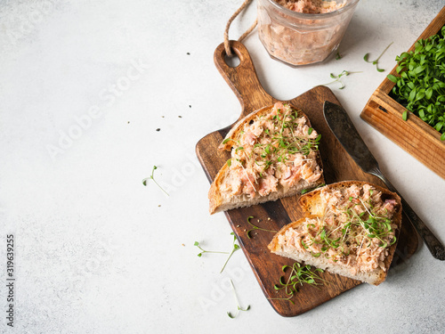 Healthy toasts with salmon pate and fresh green sprouts on yeast-free bread on wood cutting board on grey background. Copy space