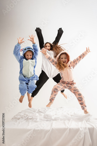 Children in soft warm pajamas colored bright playing at home. Little girls having fun, party, laughting, jumping together, look stylish and happy. Concept of childhood, leisure activity, happiness.