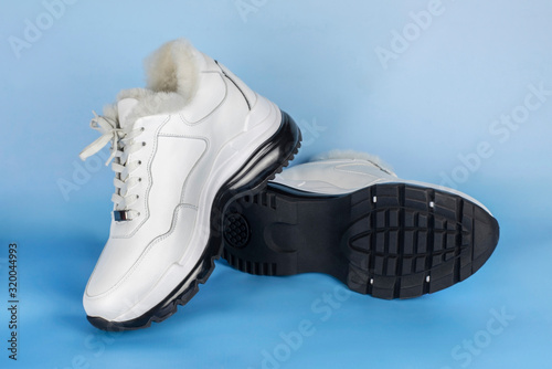 White women's low boots with white fur on a blue background. Warm shoes for women and girls who love sports shoes