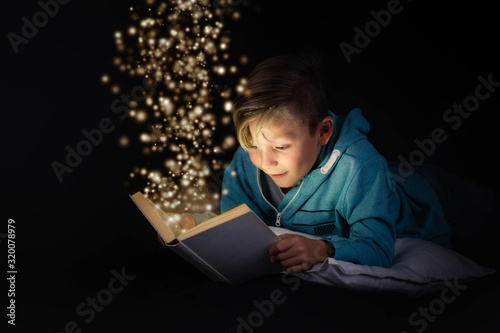 blond boy reading a magicical story book with light leaping off the page