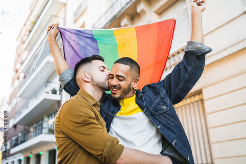 Gay couple embracing and showing their love with rainbow flag.