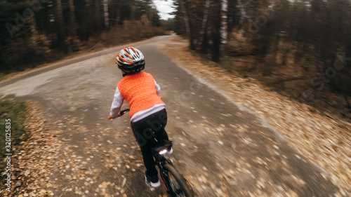 One caucasian children rides bike road in autumn park. Little girl riding black orange cycle in forest. Kid goes do bicycle sports. Biker motion ride with backpack and helmet. Mountain bike hard tail.