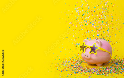 A pink piggy bank in fun glasses at a party. Yellow background.