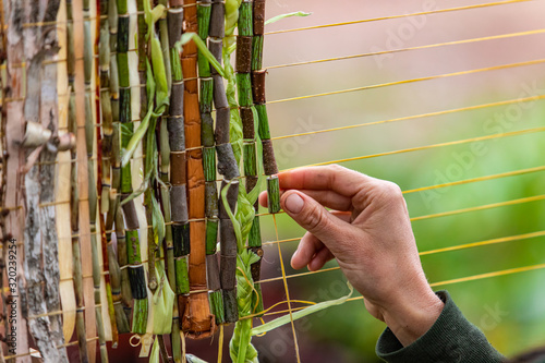 Closeup cropped image of human hand decorating yellow string with green braided leaves and wooden bamboos wampum during world and spoken word festival