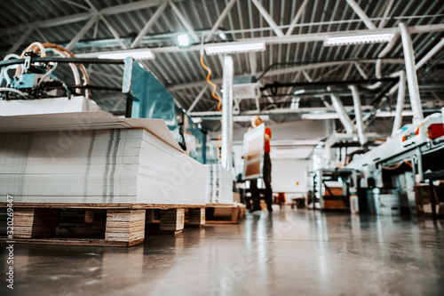 Low angle view of piles of sheets in printing shop. In background are worker and printing machines.