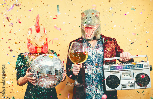 Crazy couple celebrating new year eve wearing chicken and dinosaur t-rex mask - Young trendy people having fun drinking champagne and listening music with vintage boombox - Absurd and holidays concept