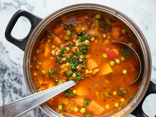 Home made Italian winter minestrone soup with winter squash, carrots, kale, green beans, peas, tomatoes and barley