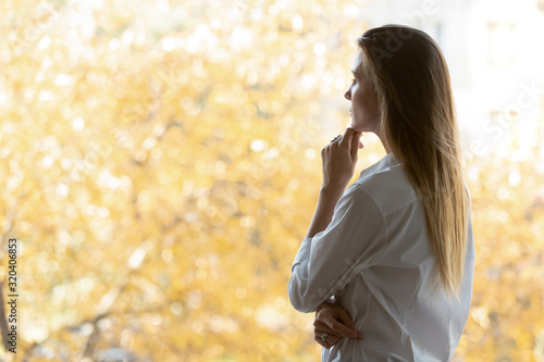 Pensive businesswoman standing in office looking out window search solution