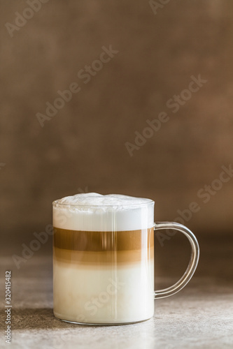 A glass of caffe latte macchiato coffee, vertical with brown background.