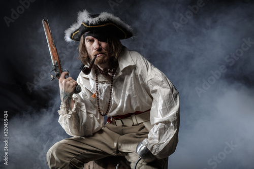 medieval bearded pirate with a sword and gun. concept photo of handsome man in a pirate vintage costume with pistol and saber