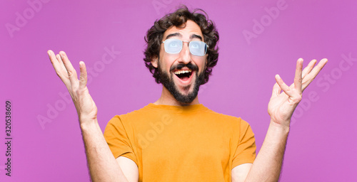 young crazy cool man feeling happy, amazed, lucky and surprised, celebrating victory with both hands up in the air against flat wall