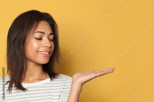 Happy black woman showing empty open hand for advertising marketing or product placement on yellow background