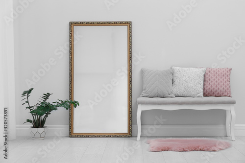 Modern large mirror and comfortable bench near light wall in room