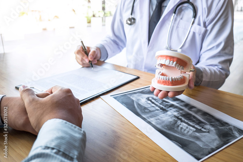 Professional Dentist showing jaw and teeth the x-ray photograph and discussing during explaining the consultation treatment issues with patient and writing history list on report