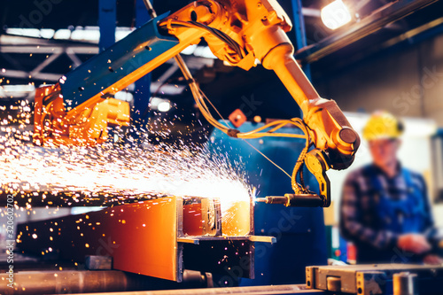 Worker controls robotic arm to cut steel in a factory.