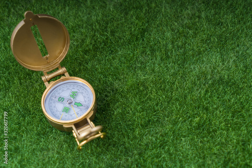 Golden old compass on green grass background. The concept of tourism, orientation, navigation. Copy space