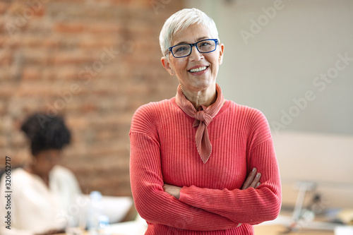 Pretty older business woman, successful confidence with arms crossed in financial building. Cheerful attractive businesswoman crossing arms on chest and looking at camera.