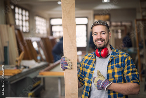 Portrait of handsome smiling carpenter with wood material at workshop holding thumbs up. Do it yourself concept. Creativity concept.