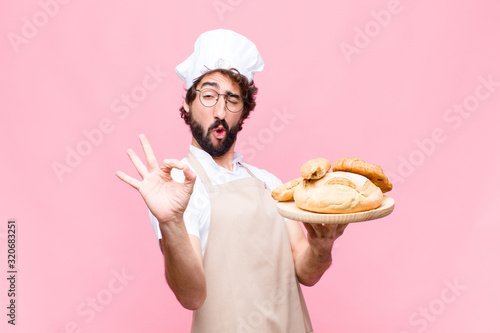 young crazy baker man holding bread against pink wall