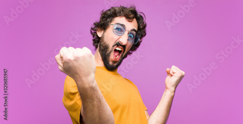 young crazy cool man shouting triumphantly, looking like excited, happy and surprised winner, celebrating against flat wall