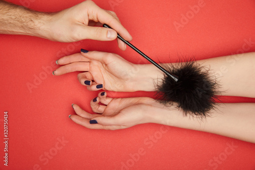 cropped view of man tickling female hands with feather tickler isolated on red