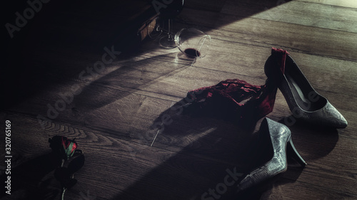 Low key photography of red wine glasses and rose with high heel and panties thrown on the floor romantic erotic lovers night