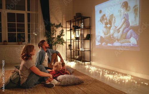 family mother father and children watching projector, TV, movies with popcorn in evening at home.