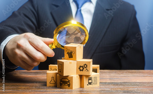 A businessman examines boxes goods with magnifying glass. Market structure research, find unoccupied target consumer niches, demand assessment. Marketing sales promotion strategy. Retailer