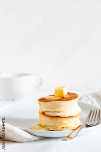 Fluffy Japan souffle pancakes, hotcakes with butter and maple syrup or honey sauces on light white background with copy space. Trendy asian food for breakfast. Vertical orientation