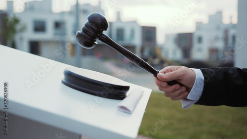 Property auction on real estate. Close-up auctioneer banging with mallet gavel by tribune outdoors. Auction bid sale jughment.