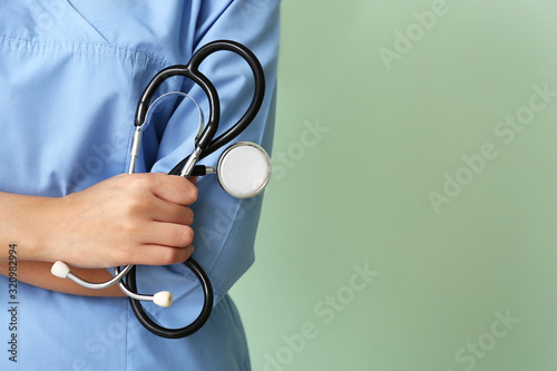 Young African-American nurse with stethoscope on color background, closeup