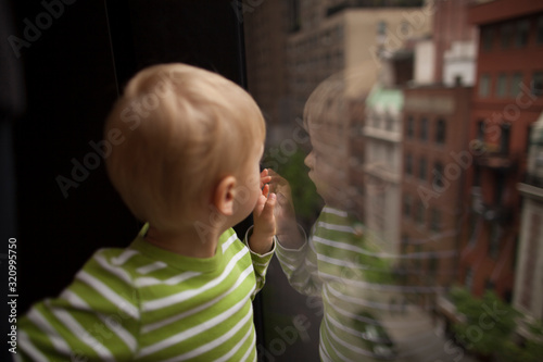 Loneliness in a big city concept. Little boy reflection in the window glass