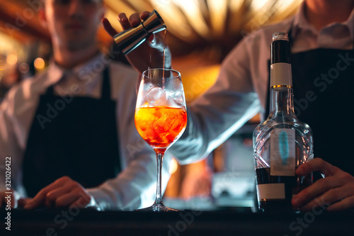 Barman hand stirring a fresh and sweet orange summer cocktail with a spoon on the bar counter.