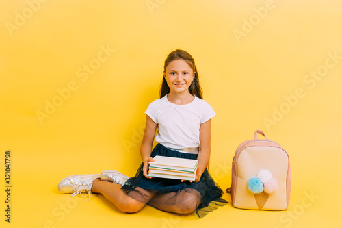 Happy teenage schoolgirl with books on a yellow background
