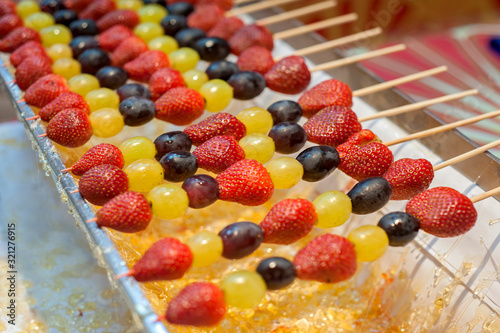 Penang, Malaysia - January 21, 2020 : Tanghulu traditional Chinese hard caramel coated strawberry skewers with grapse, also called bing tanghulu candied hawthorn sticks.