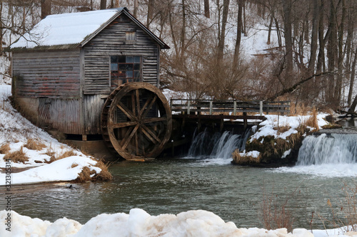 Rural landscape with old abandoned watermill in woods. Snowy winter view of obsolete wooden mill and waterfall between trees. Travel America, Wisconsin, Midwest USA.