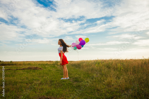 Teenage girl with colourful balloons stands outdoor