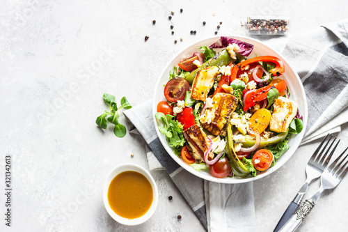 Vegetable salad cherry tomatoes, baked pepper, salad mix and onion with grilled haloumi (halloumi) cheese. Keto diet, healthy food. Light grey stone background. Top view.