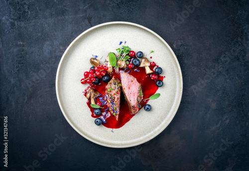 Fried dry aged venison tenderloin fillet medallion steak natural with mushrooms and forest berries as closeup on a modern design plate with copy space