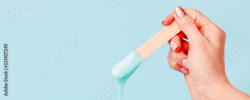 depilation and beauty concept - sugar paste or wax honey for hair removing with wooden waxing spatula sticks in hand on blue background, copy space, beauty industry, concept of smooth skin remove